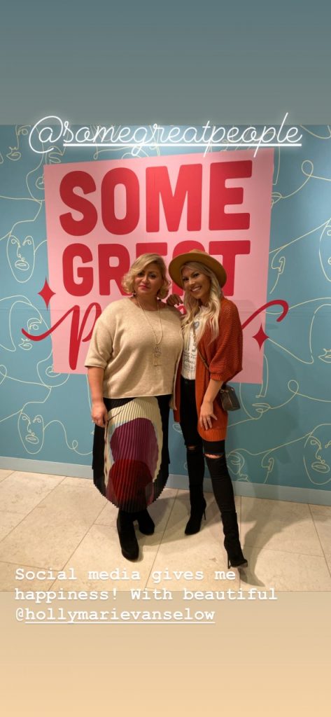 Two women posing in front of a colorful wall with the words "Some Great".