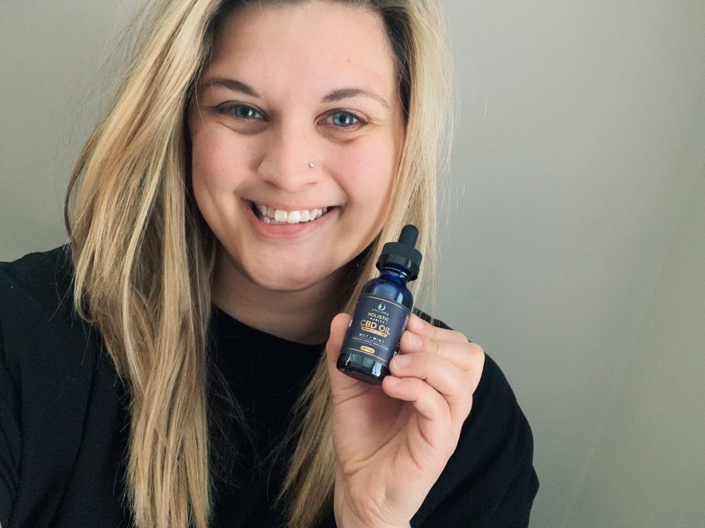 Smiling woman holding a small blue bottle of product, showcasing it to the camera.