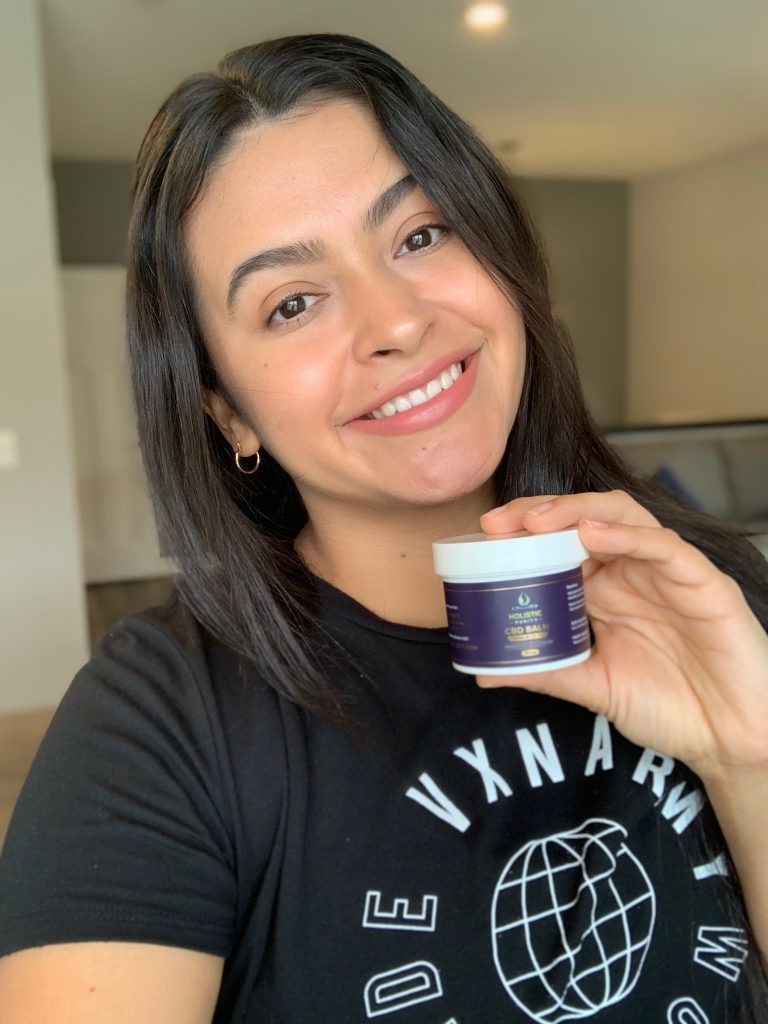 A smiling woman holding a skincare product jar indoors.