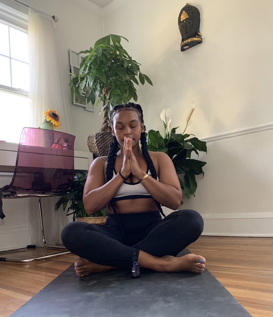 Young woman meditating peacefully in a bright room surrounded by plants.